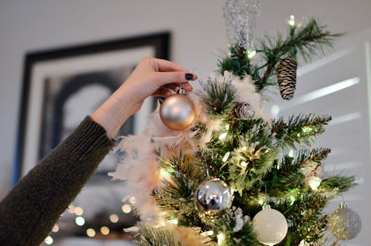 A hand decorates a Christmas tree with shiny ornaments, capturing the festive spirit.